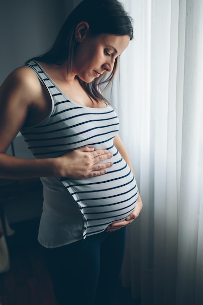 Pregnant woman looking her belly in front of a curtain