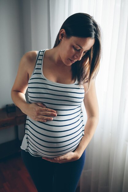 Pregnant woman looking her belly in front of a curtain