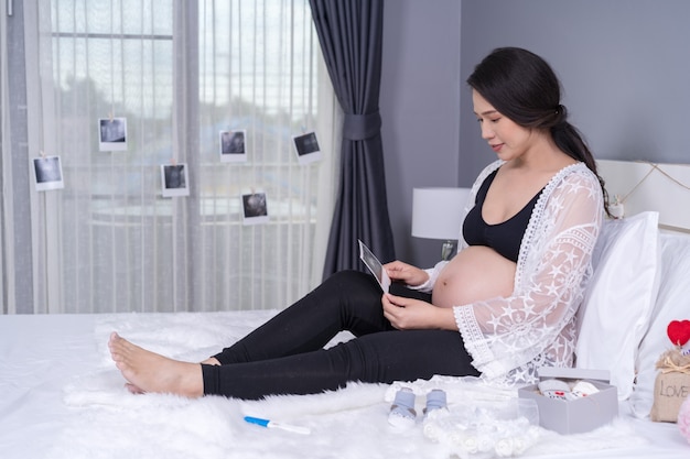 Pregnant woman looking ultrasound photo on bed