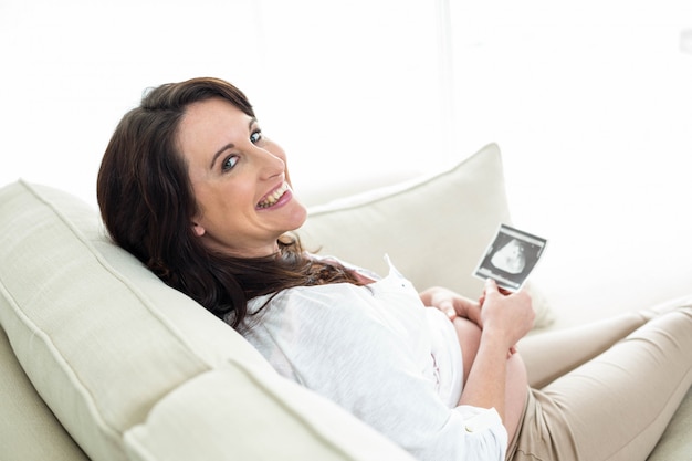 Pregnant woman looking at ultrasound scans on couch