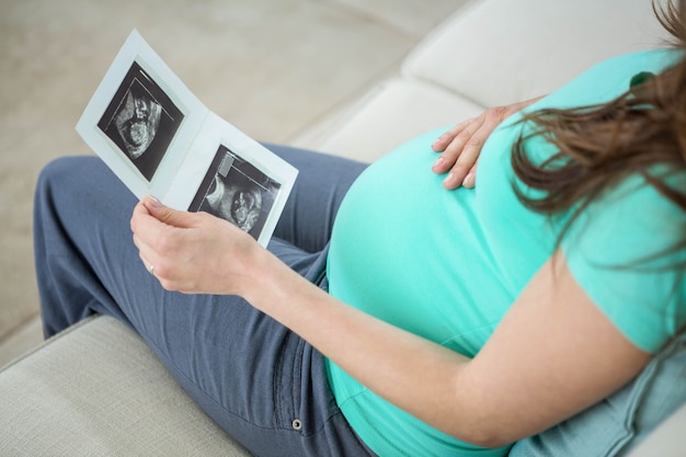 Pregnant woman looking at ultrasound scans on couch