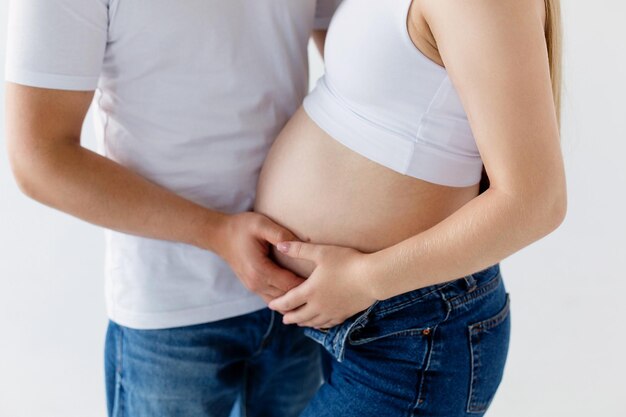 Photo a pregnant woman and a loving husband hugs her stomach on a white background the feeling of the baby's movement by a couple on the pregnant woman's stomach closeup