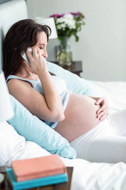 妊娠中の女性が彼女の寝室で電話をかけるベッドで横になっています。