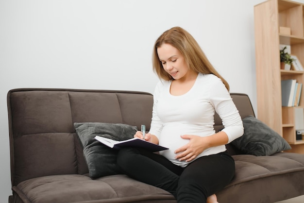 Pregnant woman lying on the sofa and making notes in her diary she resting at home