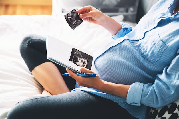 妊娠中の女性はノートにメモを取り、超音波画像と医療文書を保持しています
