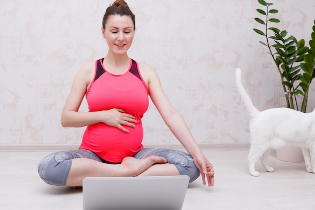 Pregnant woman makes yoga practice online class at home Looks at the laptop in yoga pose