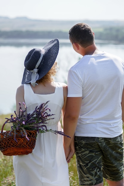 a pregnant woman and a man in white clothes and a hat with a basket stand on the Bank of the river