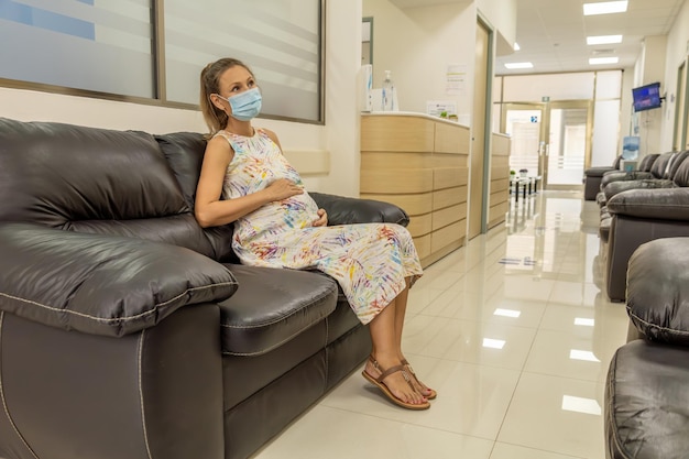 Photo pregnant woman in a mask sits on a sofa in corridor of an obg medical clinic