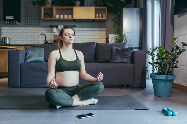Беременная женщина медитирует и занимается йогой в позе лотоса дома