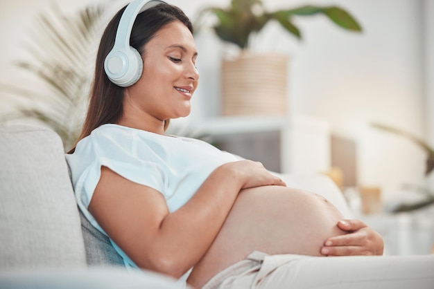 写真 妊娠中の女性の音楽と自宅でリラックスして赤ちゃんと絆を深めながら、お腹や隆起を保持する赤ちゃんの母親は、お腹に触れ、家族の家で絆を深めるためにヘッドセットでオーディオを聴きます