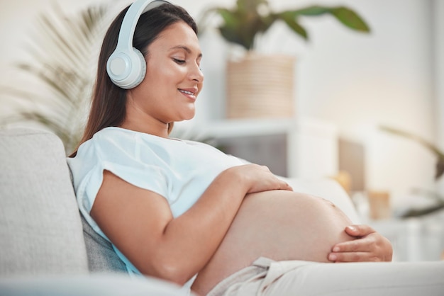 Pregnant woman music and holding belly or bump while relaxing and bonding with her baby at home Babies mother touching stomach and listen to audio on headset for bond in family home