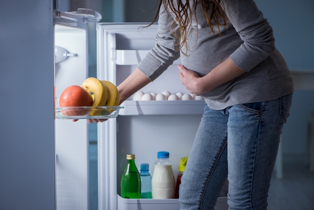 Pregnant woman near fridge looking for food and snacks at night