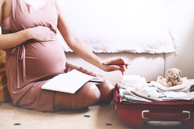 Foto borsa da imballaggio per donna incinta per l'ospedale che prende appunti sulla lista di controllo nel diario durante la gravidanza
