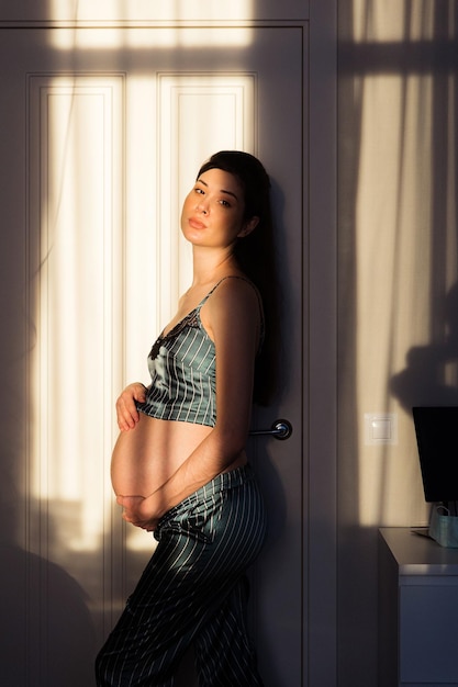 Pregnant woman in pajamas standing in the sun at home