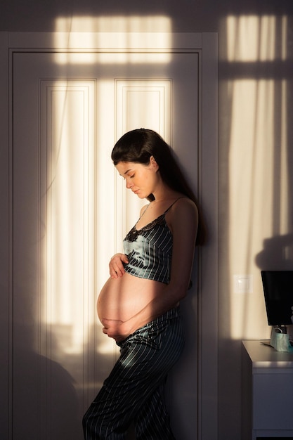 Donna incinta in pigiama in piedi al sole a casa