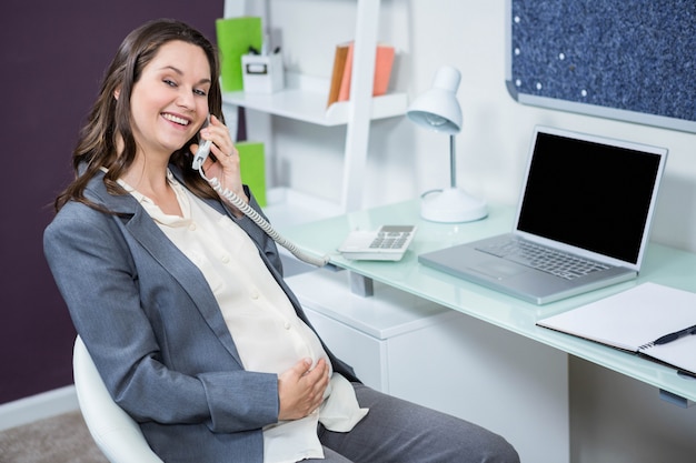 Беременная женщина по телефону в домашнем офисе