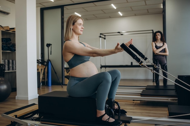 Pregnant woman pilates reformer cadillac exercise workout at gym