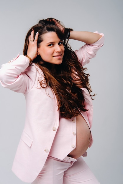 Pregnant woman in pink suit close-up on gray background