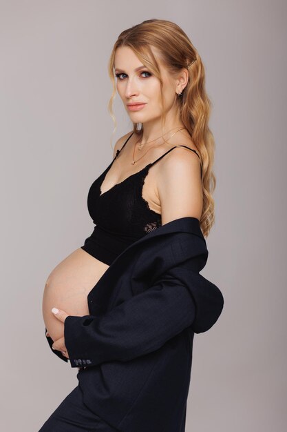 A pregnant woman poses in front of a grey background