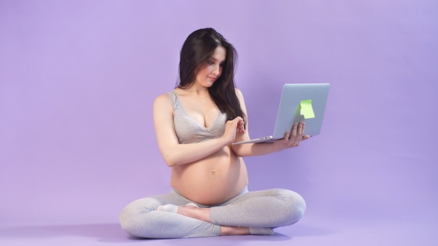 Pregnant woman poses in a Studio in comfortable home clothes. Isolated purple space.