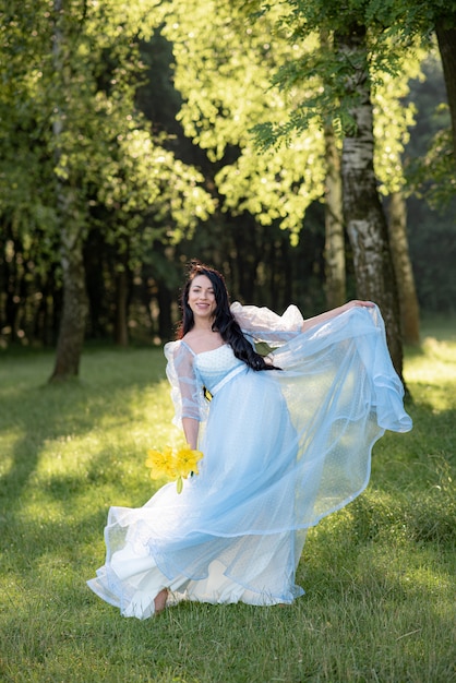 Pregnant woman posing in a blue dress on a background of green trees