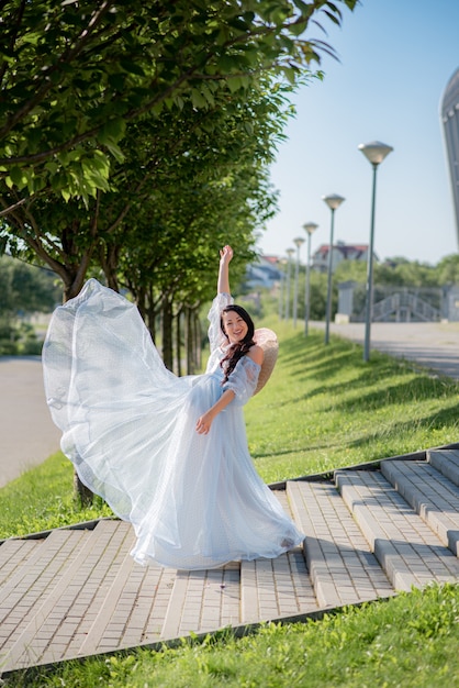 Pregnant woman posing in a blue dress on a background of green trees.