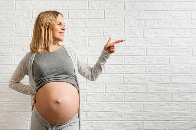 Foto donna incinta che posa davanti ad un muro di mattoni