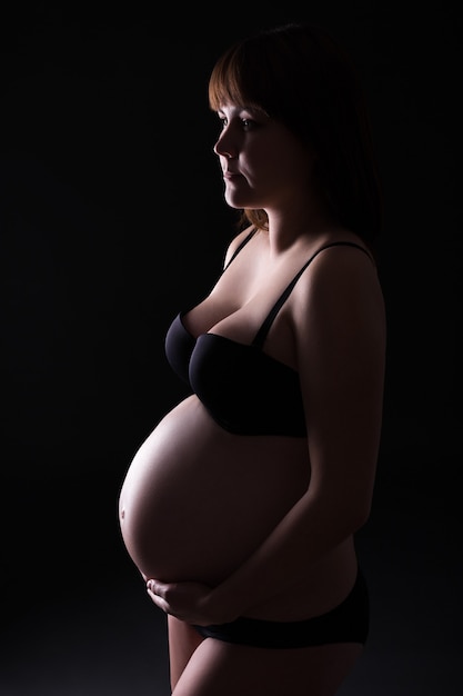 Pregnant woman posing in lingerie over black background