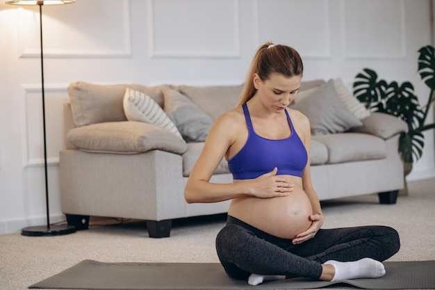 Pregnant woman practicing yoga at home on mat
