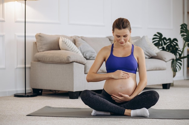 Pregnant woman practicing yoga at home on mat