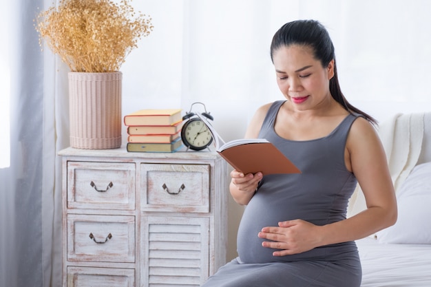 Pregnant woman reading a book and put your hand on belly. Researching information about childbirth. Mental health  care and pregnancy.