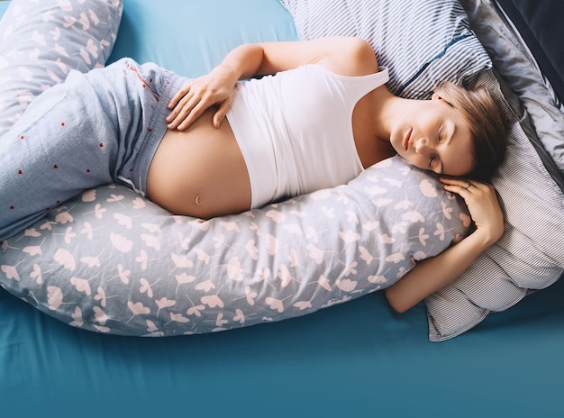 pregnant woman relaxing or sleeping with belly support pillow in bed concept pregnancy maternity