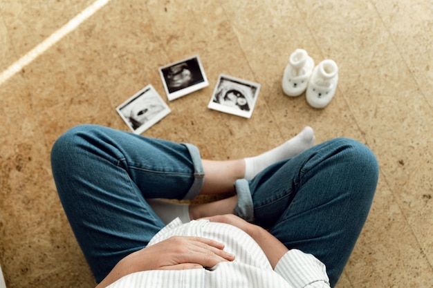 Photo pregnant woman's belly top view pregnancy ultrasound shot and baby clothes lie near a pregnant woman