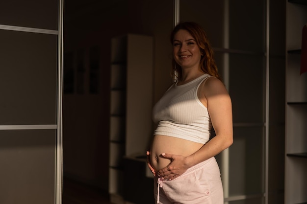 A pregnant woman in shorts and a crop top stands in profile between folding doors