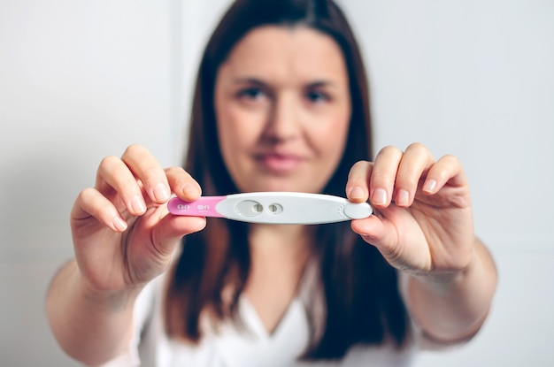 Pregnant woman showing positive pregnancy test. Selective focus on pregnancy test in foreground