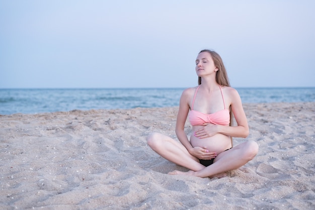 Pregnant woman sits on the beach and enjoys. Soft evening light, deserted beach.