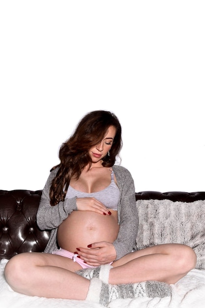 A pregnant woman sits on a couch with her belly exposed.