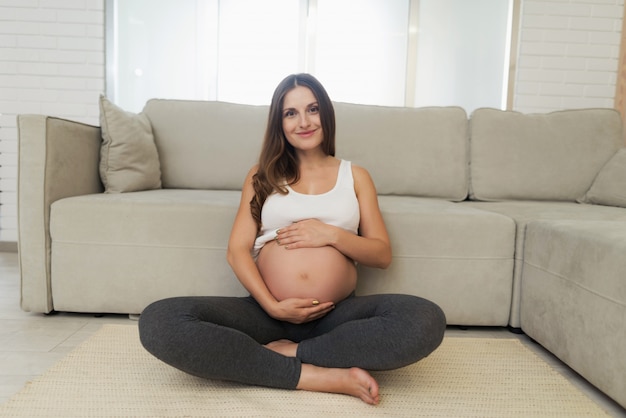 Беременная женщина сидит на полу со скрещенными ногами.