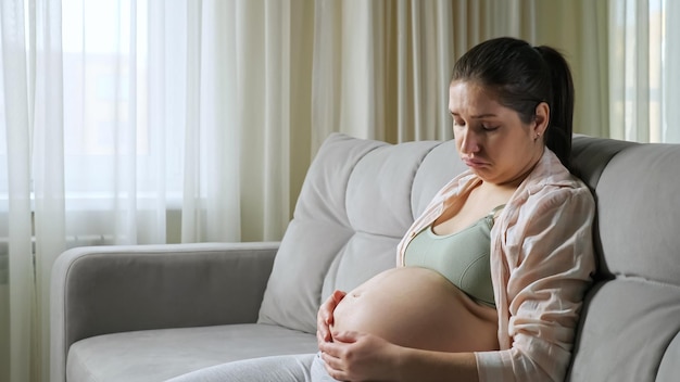 Pregnant woman sits on sofa upset from gaining weight