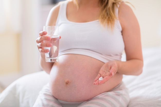 Pregnant woman sitting on bed  and holding glass of water 