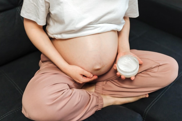 Pregnant Woman sitting on bed stroking apply cream on big belly at home