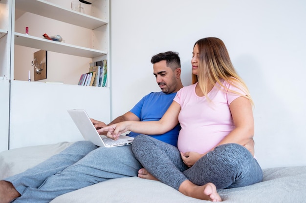 pregnant woman sitting on the bed with her husband using the laptop