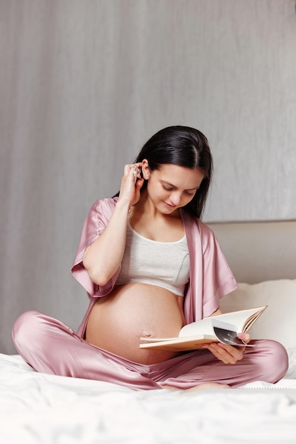 Беременная женщина сидит на кровати и пишет в блокноте
