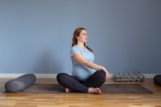 Pregnant woman sitting on floor in marichyasana stretching muscles