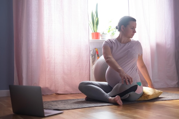 Pregnant woman sitting on floor stretching doing twisted asana at home