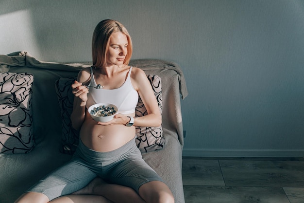 Foto donna incinta seduta sul divano e con in mano un piatto con ricotta e mirtilli