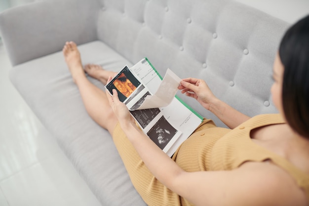 Pregnant woman sitting on the sofa and holding ultrasound picture