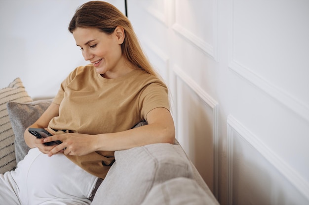 Pregnant woman sitting on the sofa at home and using phone