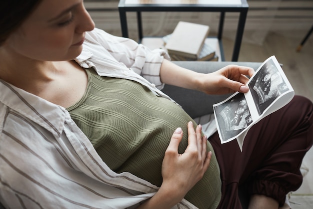 Pregnant woman sitting on sofa and resting she looking at x-ray image and waiting for the birth of her baby