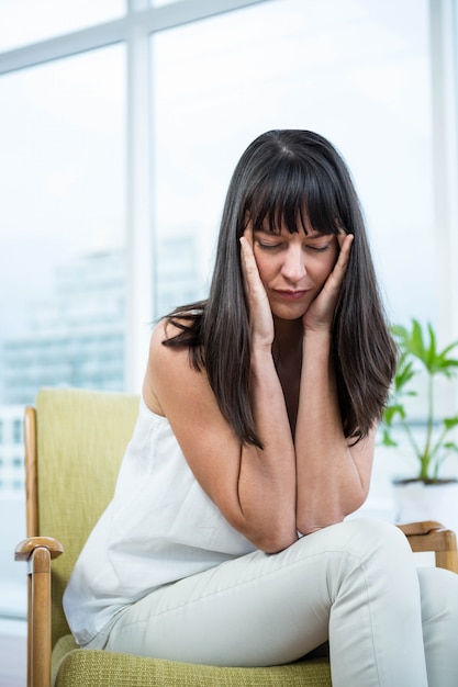 Pregnant woman sitting with headache at home